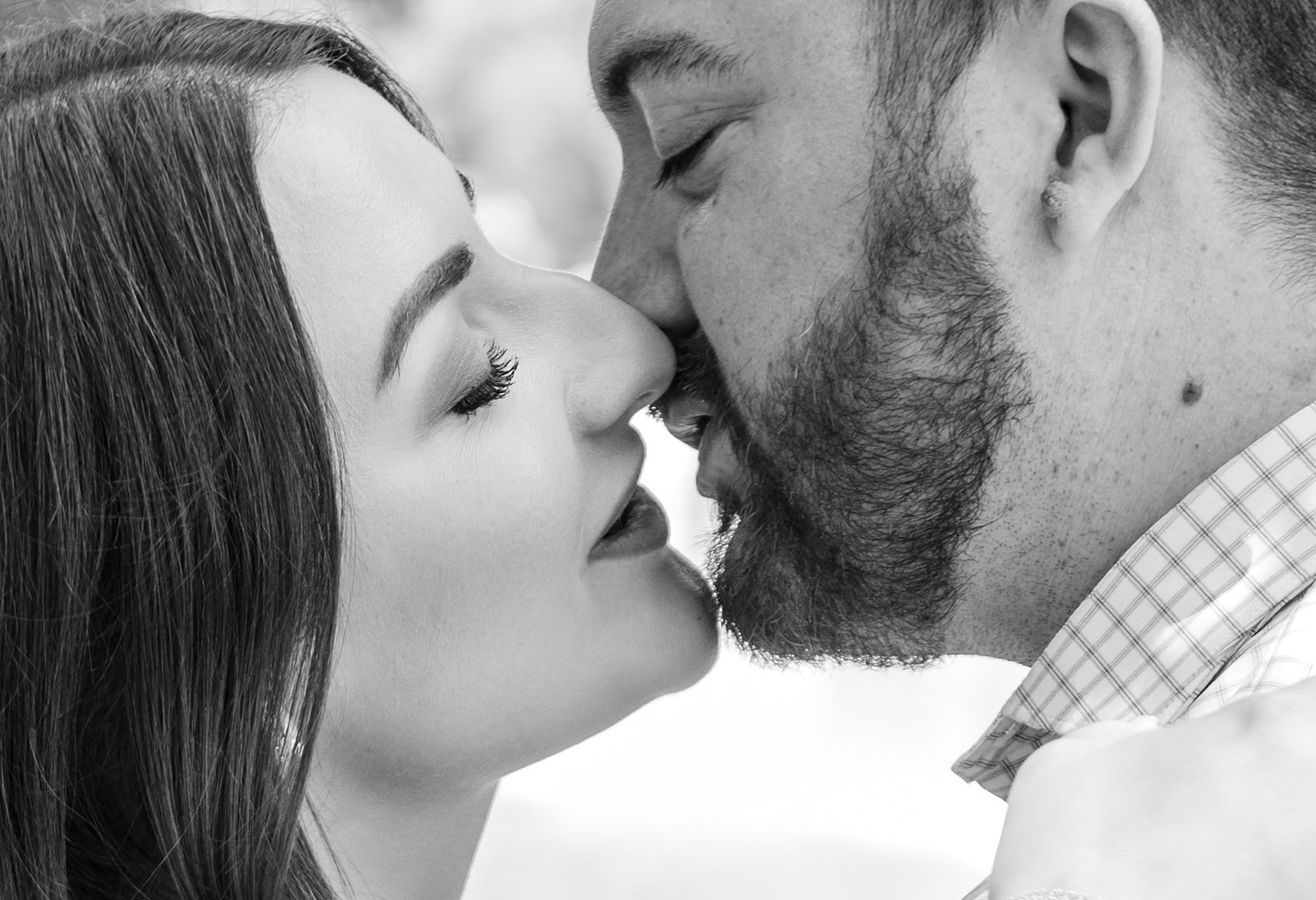 An engaged couple leans in for a kiss in this close up black and white portrait.